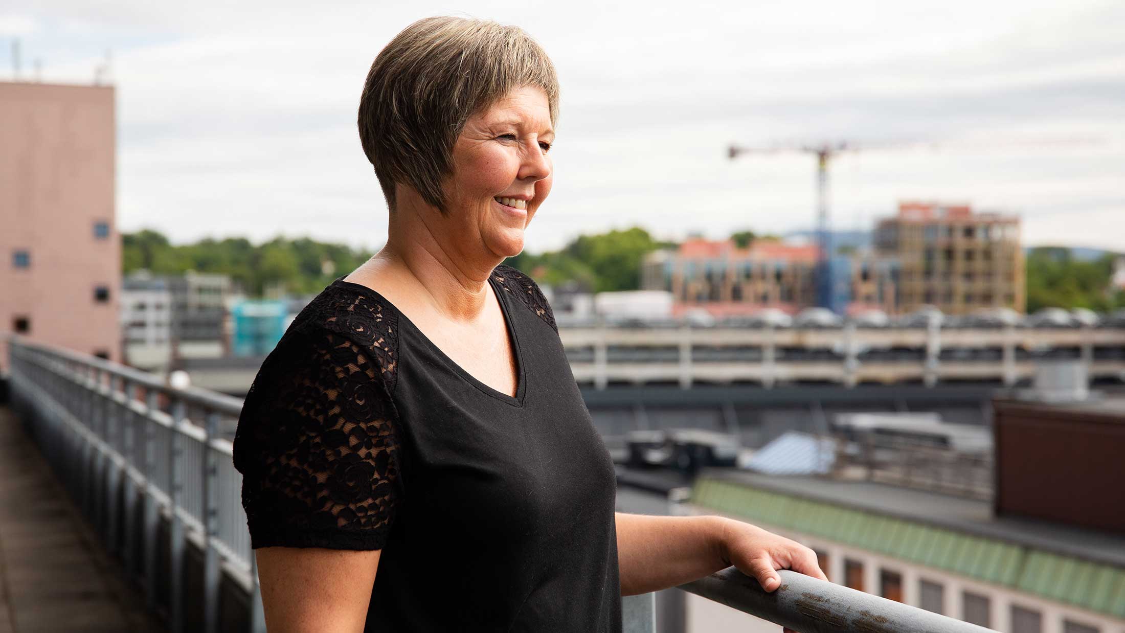 Veidekke employee standing outside on a veranda looking at the view of the urban environment