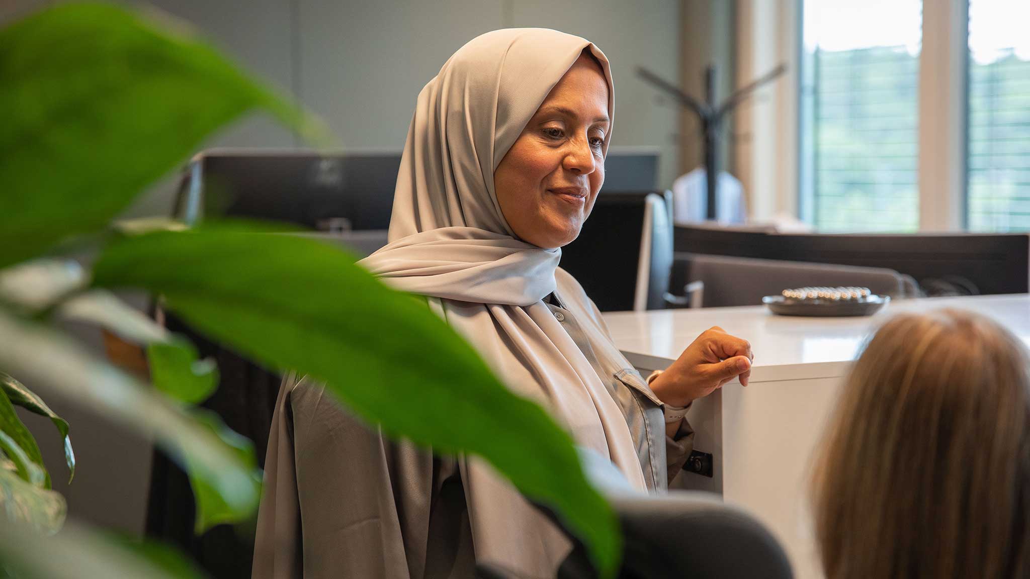 Muslim woman wearing a hijab in conversation with a colleague in an open office